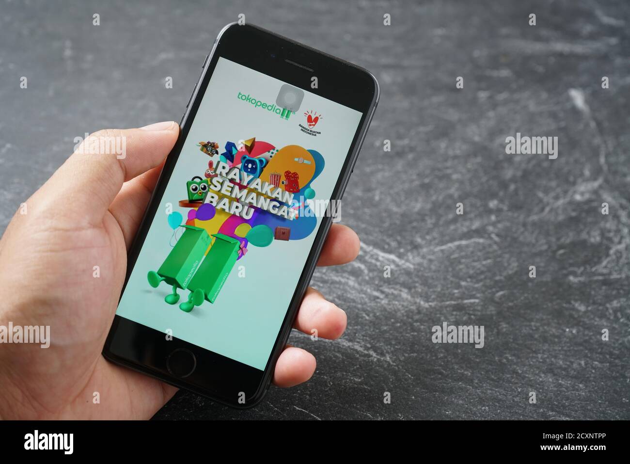 Mataram, Indonesia - 1 ottobre 2020: Mano che tiene Apple iPhone 8 con il marketplace tokopedia negozio on-line sullo schermo su pietra pad, vista dall'alto. Foto Stock