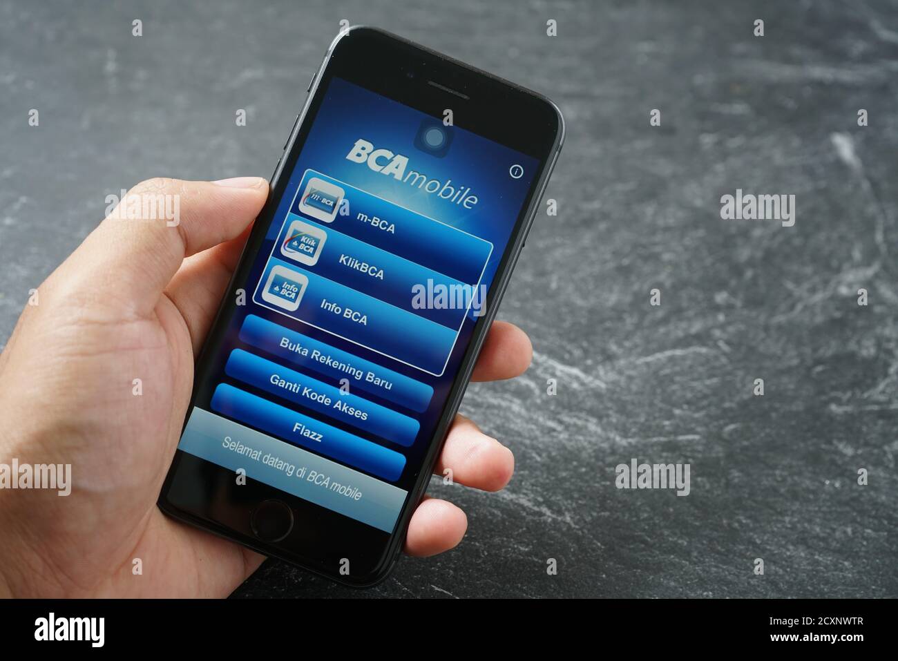 Mataram, Indonesia - 1 ottobre 2020: Mano che tiene Apple iPhone 8 con BCA mobile bangking app sullo schermo pietra pad, vista dall'alto. Foto Stock