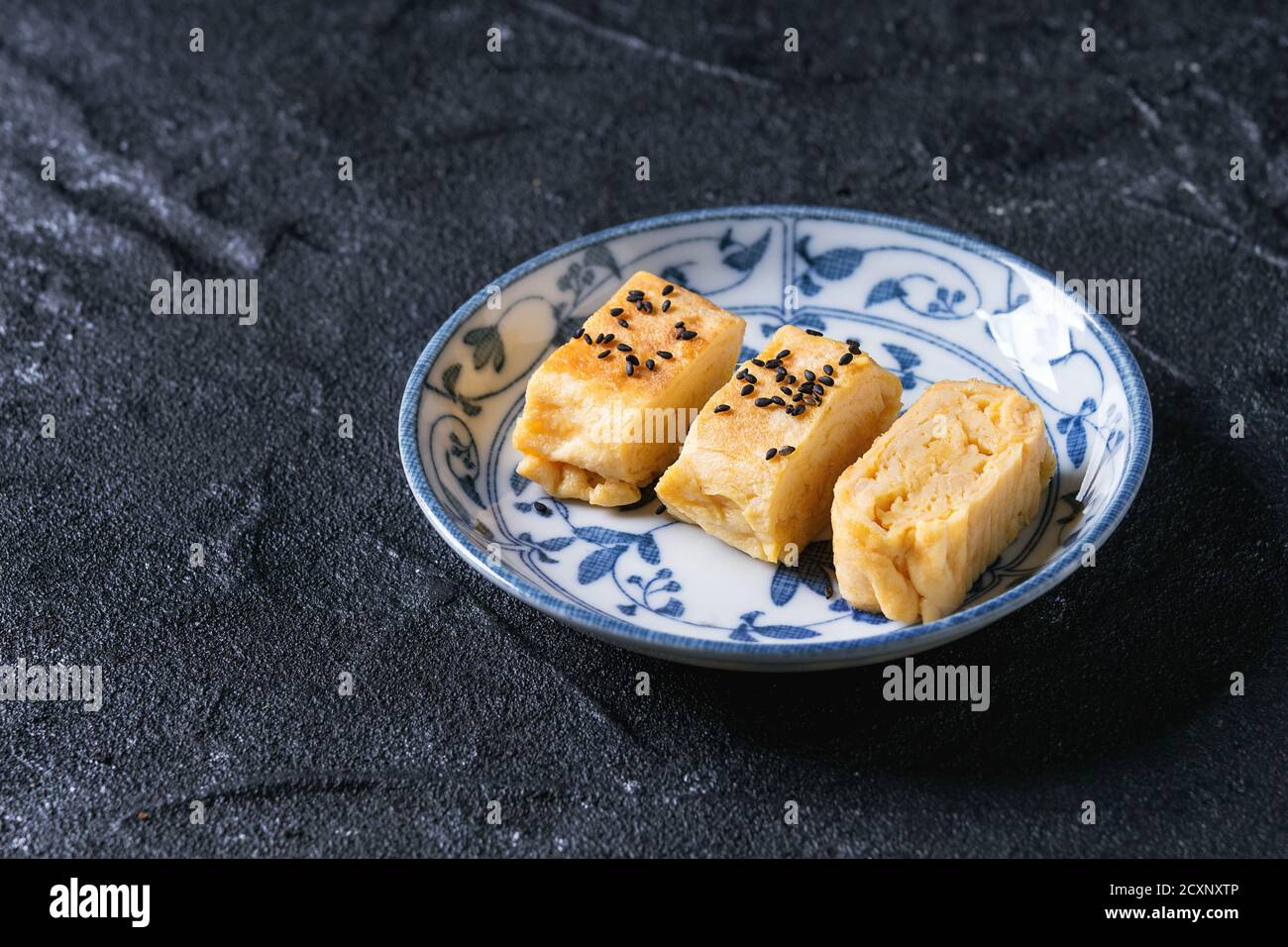 Il giapponese laminato Omelet Tamagoyaki affettato con semi di condimento nero e salsa di soia, servito in piastra di ceramica bianco blu ornato su grana di pietra nera ba Foto Stock
