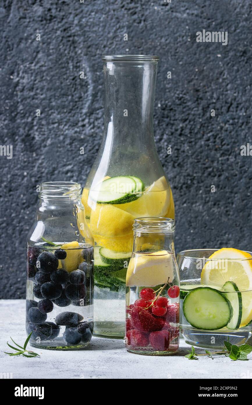 Bacche di cetrioli di agrumi, mirtillo e raspberry sassy acqua sassi per disintossicare in bottiglie di vetro su fondo grigio. Mangiare pulito, stile di vita sano Foto Stock