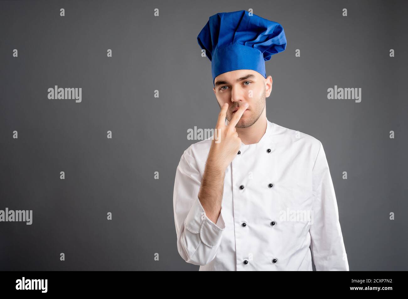 Presti attenzione o guardi me il concetto con il maschio giovane vestita con un vestito bianco da chef che si posa su un grigio sfondo con area di pubblicità dello spazio di copia Foto Stock