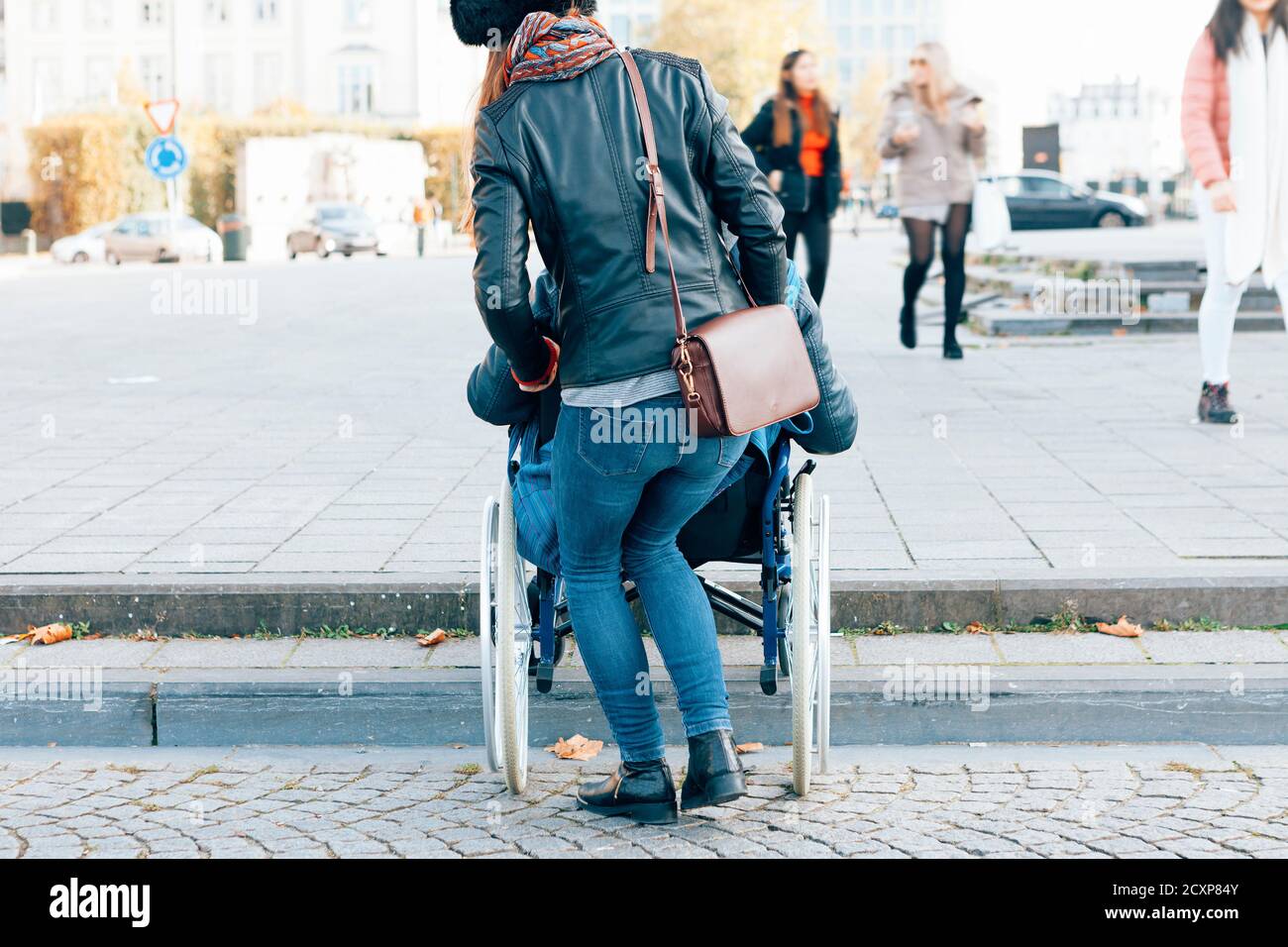 vista posteriore di una donna che aiuta una persona disabile a. scendete i gradini con la sedia a rotelle - confini architettonici nel concetto di città Foto Stock