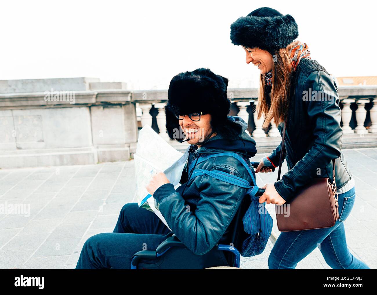 coppia sorridente ottimista che cammina per strada con una sedia a rotelle Foto Stock
