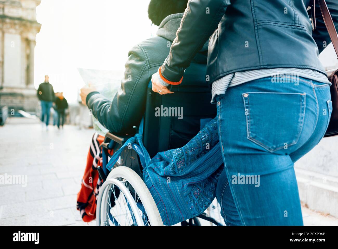 vista laterale di un uomo seduto in una sedia a rotelle una mappa nelle sue mani mentre una donna dentro un abbigliamento casual lo spinge a paround la città Foto Stock