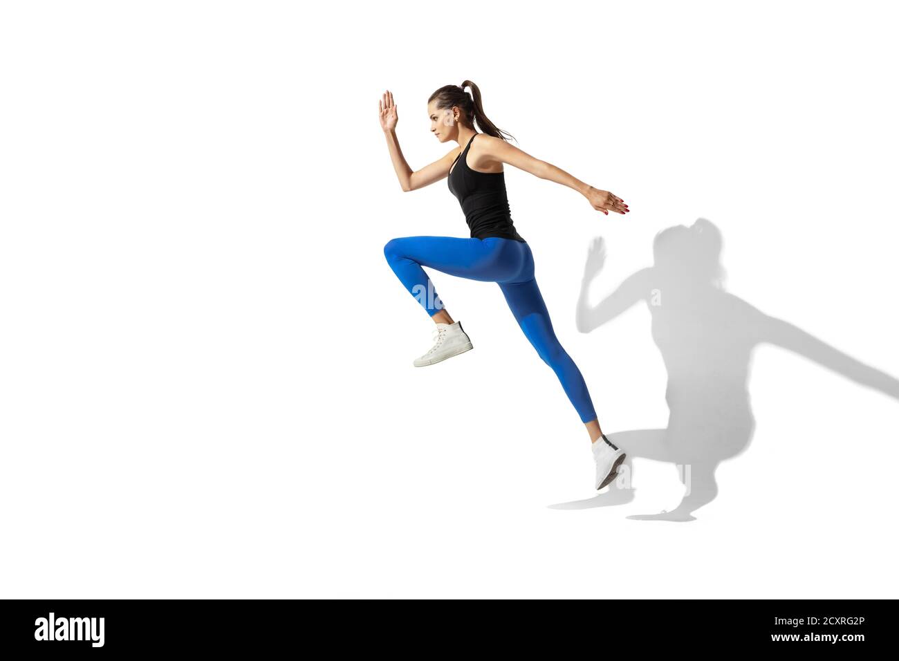 Alto. Bella giovane atleta stretching, allenamento su sfondo bianco studio, ritratto con ombre. Modello sportivo in movimento e azione. Flessibilità, stile di vita sano, concetto di stile. Foto Stock