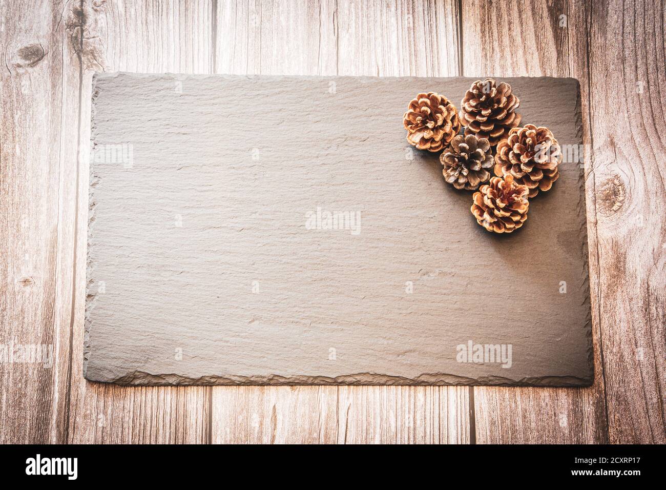 Coni di pino su un'ardesia poggiante su uno sfondo di legno con spazio di copia, uno sfondo di autunno Foto Stock