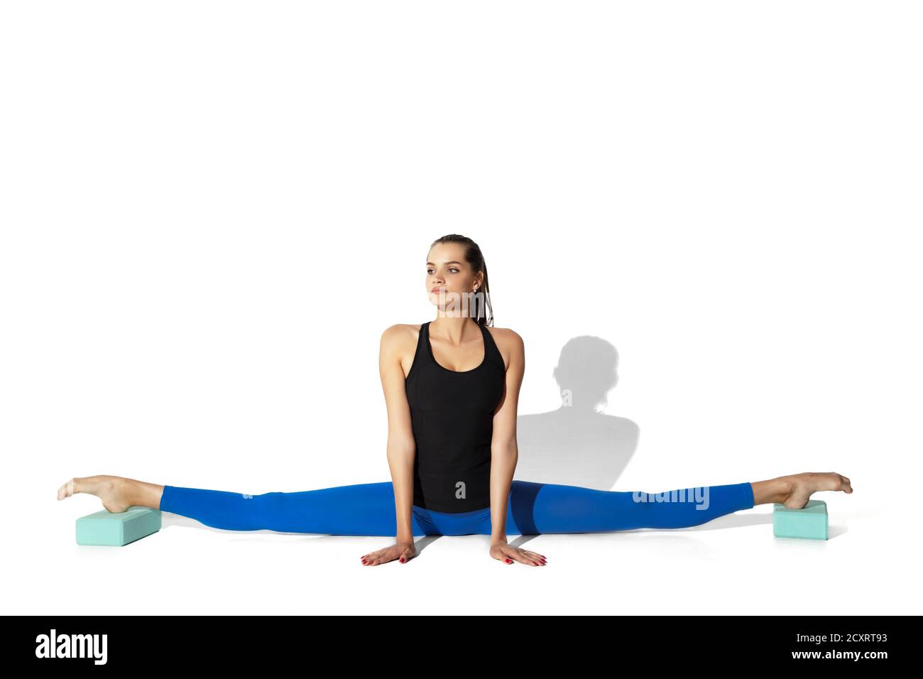 Forte. Bella giovane atleta stretching, allenamento su sfondo bianco studio, ritratto con ombre. Modello sportivo in movimento e azione. Flessibilità, stile di vita sano, concetto di stile. Foto Stock