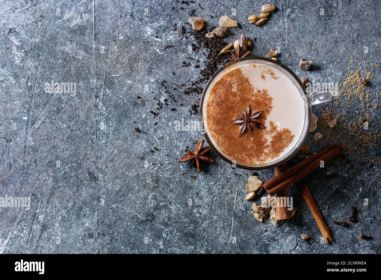 Bicchiere di vetro di tradizionale indiano Masala chai tè con gli ingredienti di cui sopra. La cannella, cardamomo, anice, zucchero, tè nero più scuro dello sfondo texture. Parte superiore Foto Stock