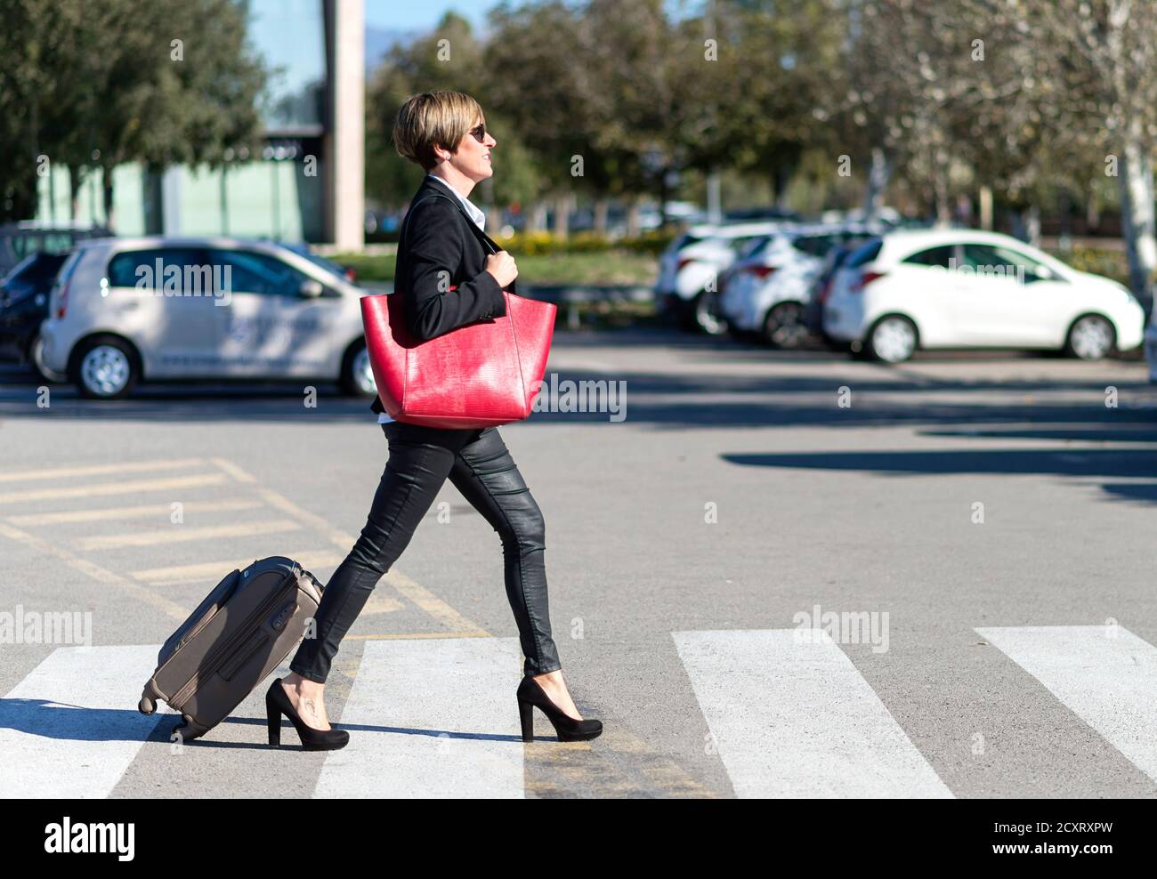 Vista orizzontale della donna d'affari allegra che trasporta i bagagli tenendo una borsa a spalla rossa Foto Stock