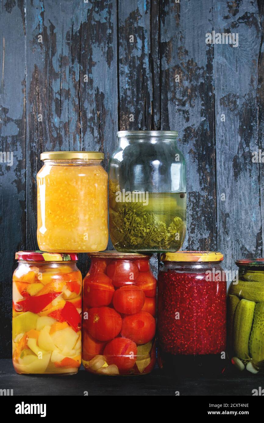 Varietà di vasi in vetro di fatti in casa o in salamoia le verdure fermentate e confetture in fila con il vecchio blu scuro tavolato in legno sfondo. Conserva stagionali. Foto Stock