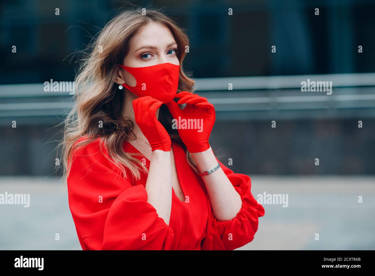 Giovane donna in abito rosso e guanti mette su medico maschera facciale Foto Stock