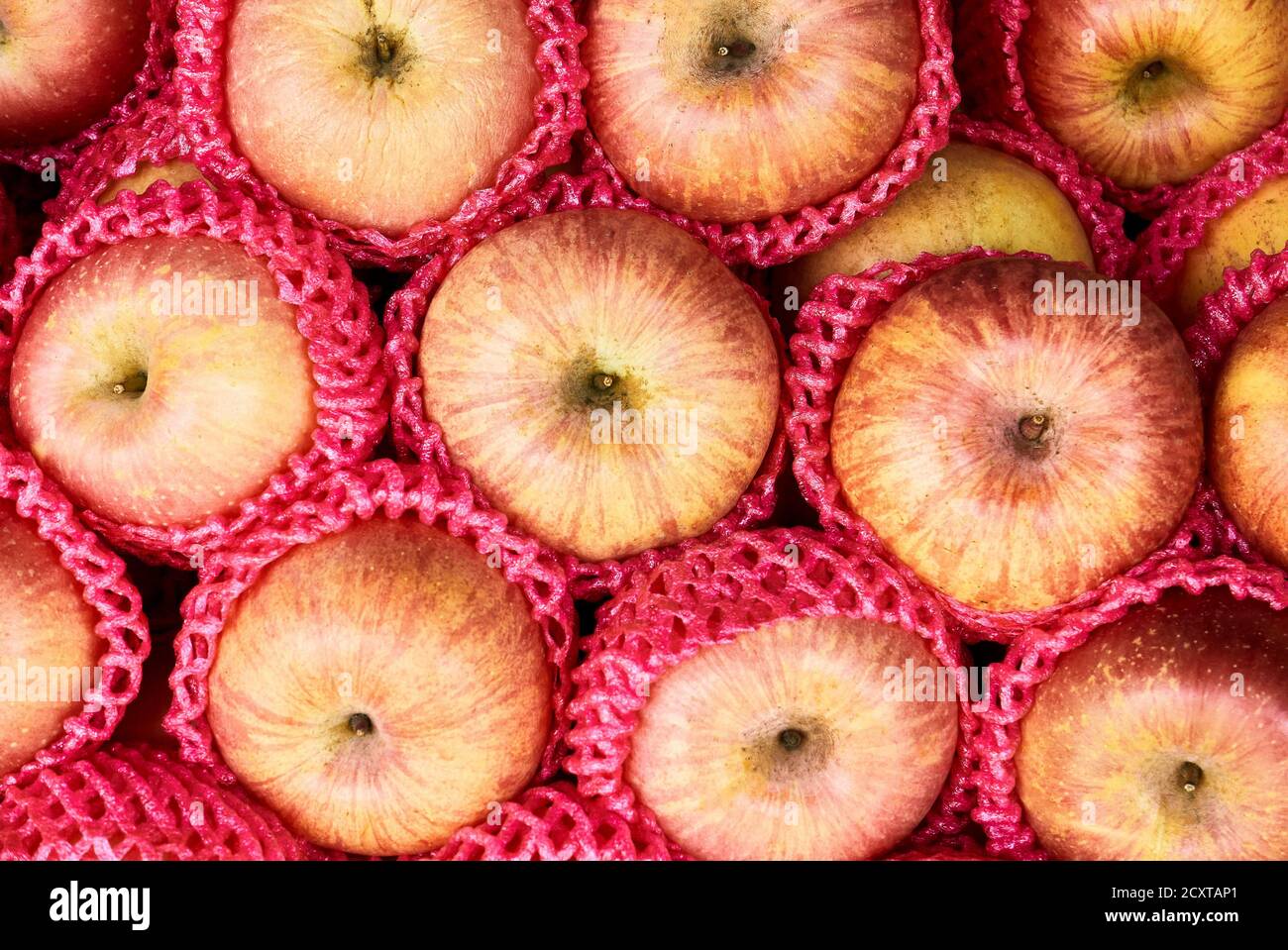 Primo piano di un mucchio di mele di colore giallo e rosso provenienti dalla Cina, confezionate singolarmente in protezioni per reti di plastica, che aggiungono un ambiente di tour dei rifiuti di plastica Foto Stock