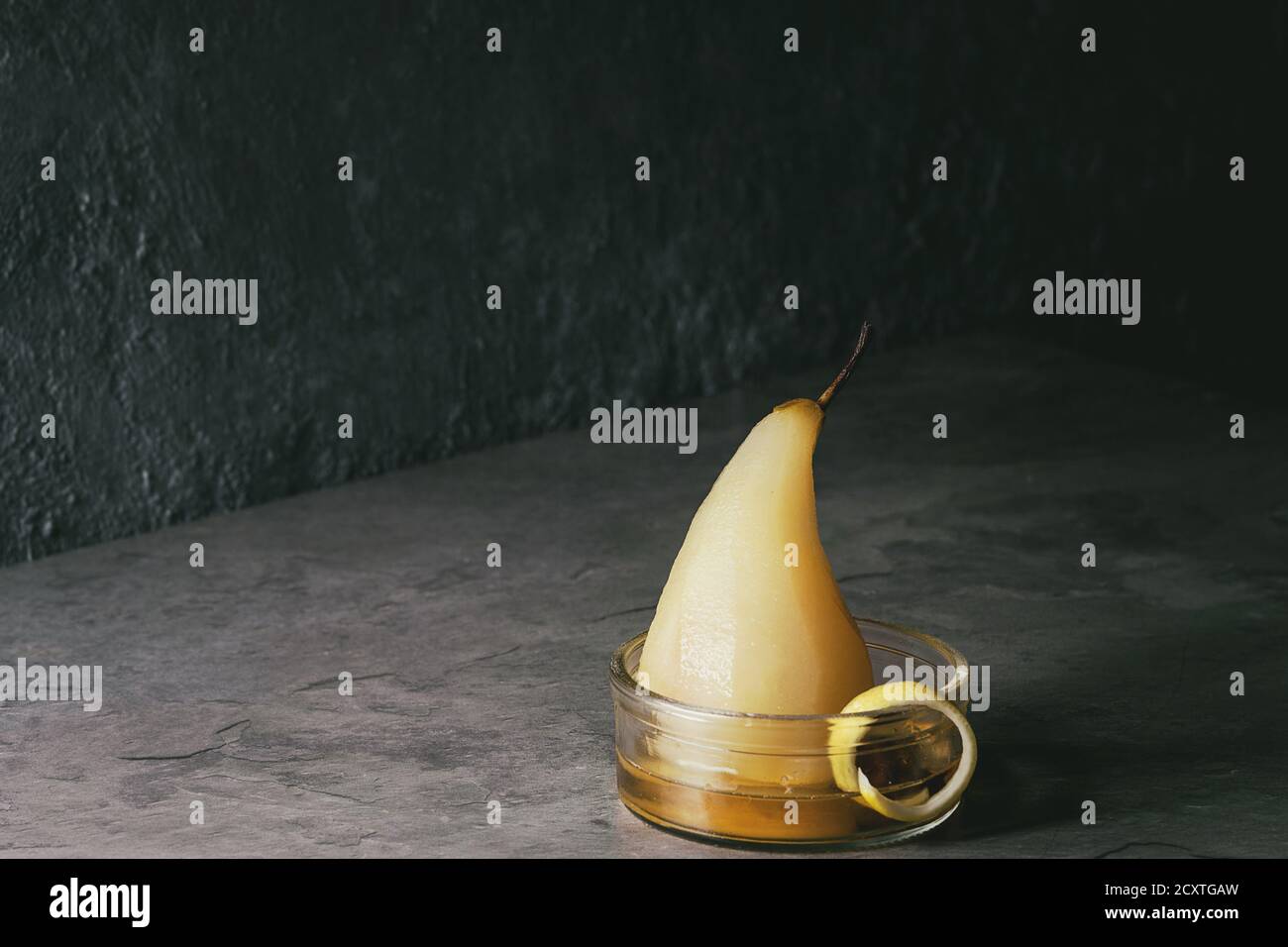 Dolce tradizionale di pera affogata nel vino bianco servito in recipiente di vetro con sciroppo e la scorza di limone su grigio tabella di texture. Foto Stock