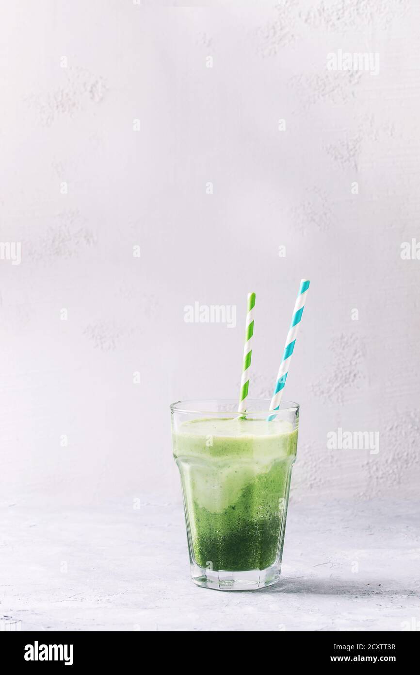 Bicchiere di tre lo strato di colore verde spinaci kale apple frullato di yogurt con cocktail retrò tubi su sfondo grigio. Vegano sano detox mangiare. Copia s Foto Stock