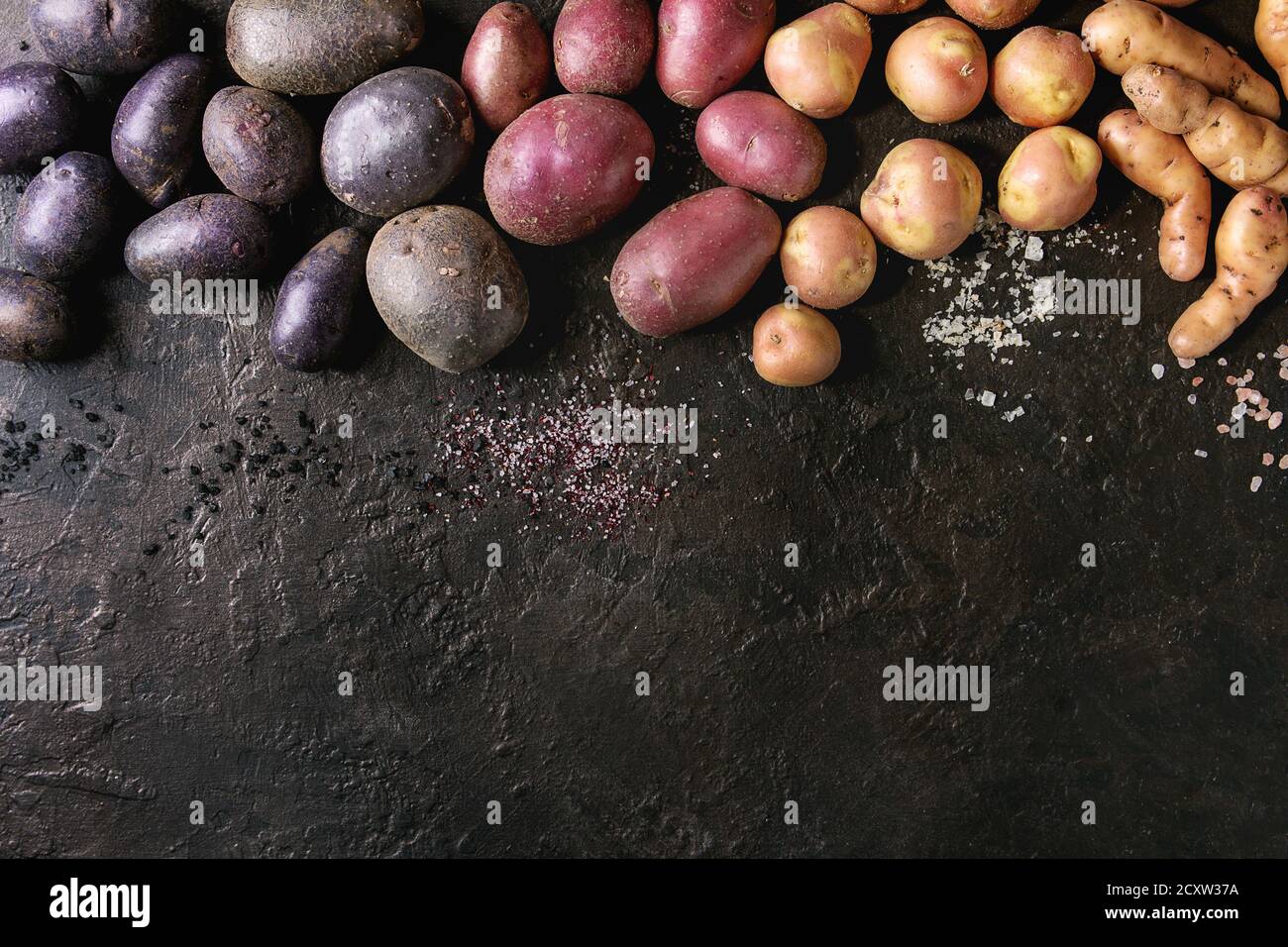 Varietà di materie organiche non cotte patate diversi tipi e colori rosso, giallo e viola con vari di sale più scuro dello sfondo texture. Vista superiore, co Foto Stock