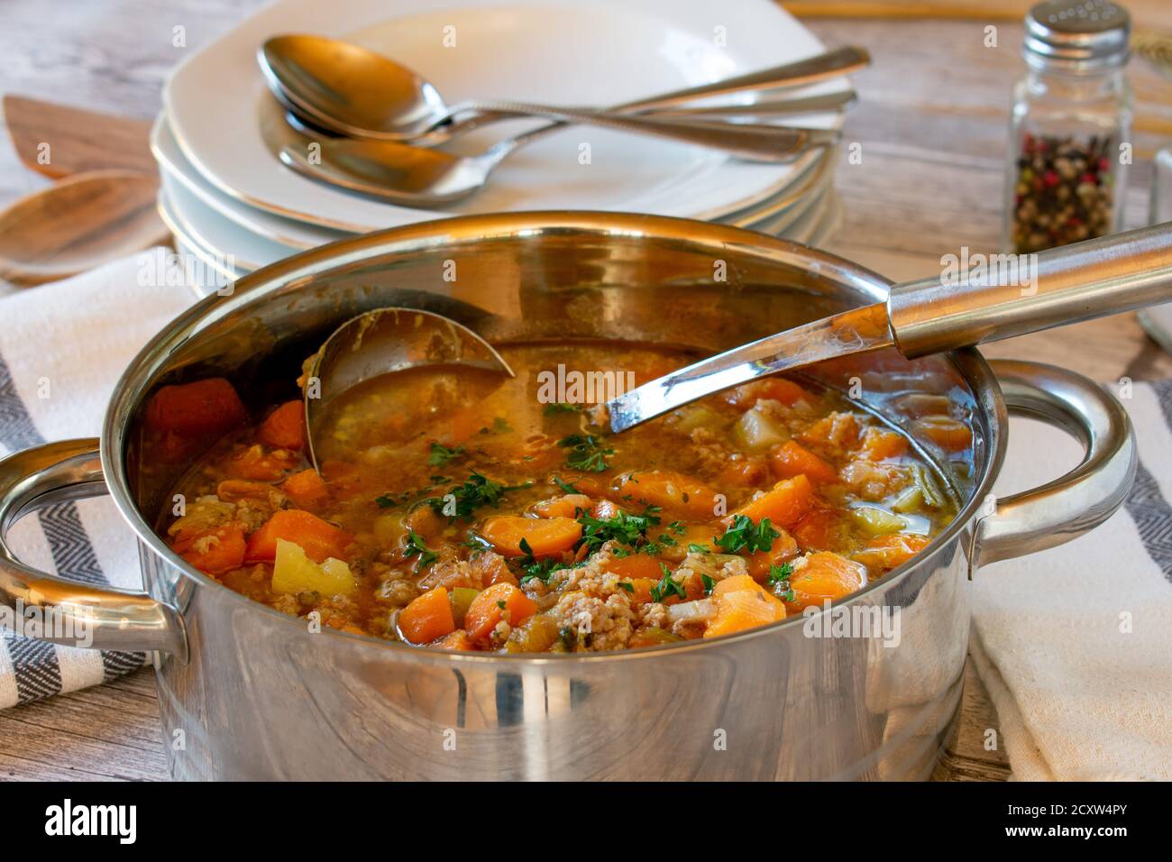 zuppa di verdure con carne tritata in una pentola con mestolo su tavolo di legno Foto Stock