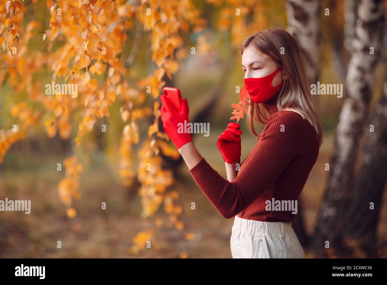 Giovane donna attiva in guanti rossi e maschera viso a. parco autunnale con telefono cellulare Foto Stock