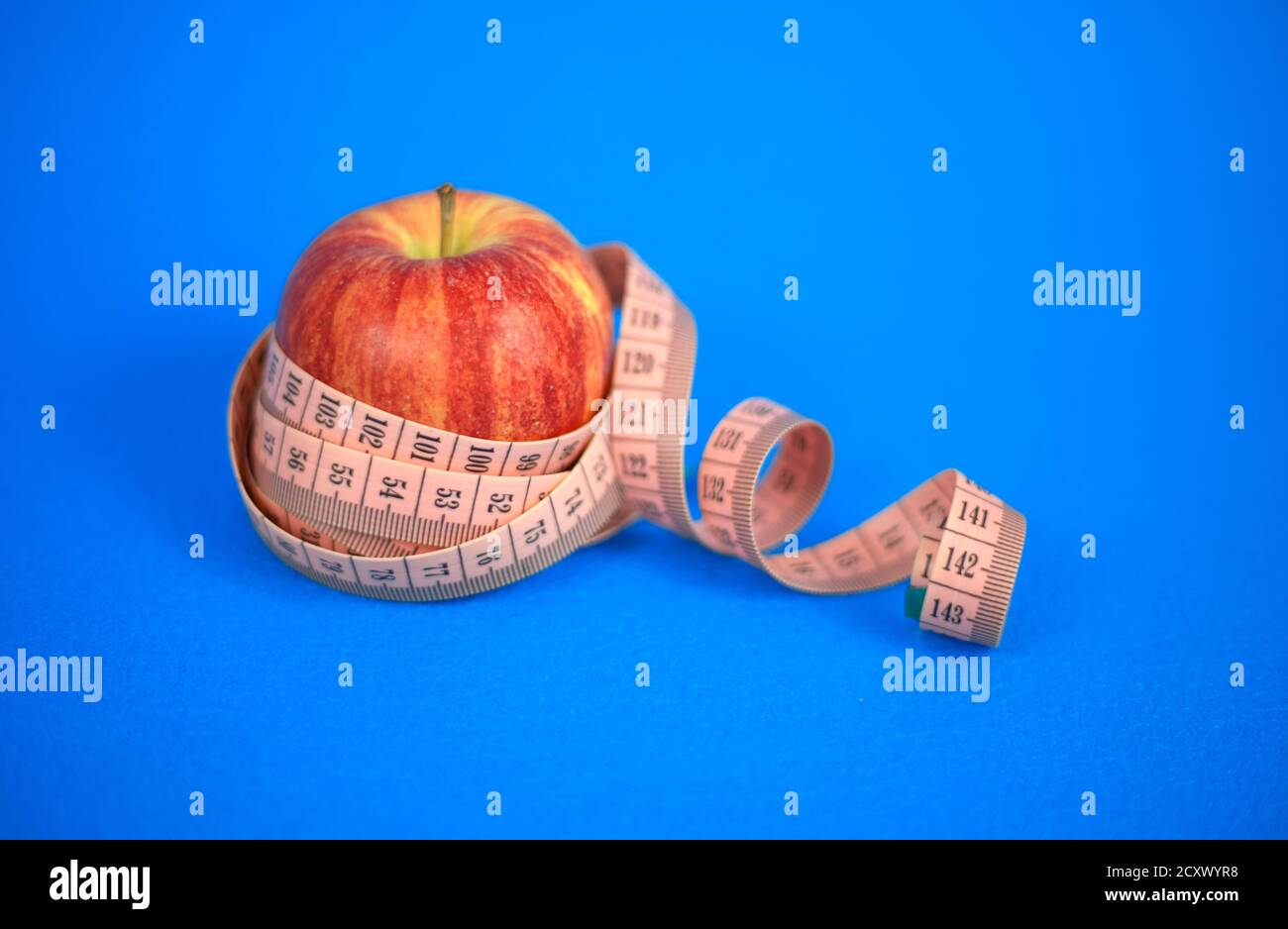 Una mela al giorno per la vostra salute. Mela rossa con nastro centimetrico su sfondo blu. Foto Stock