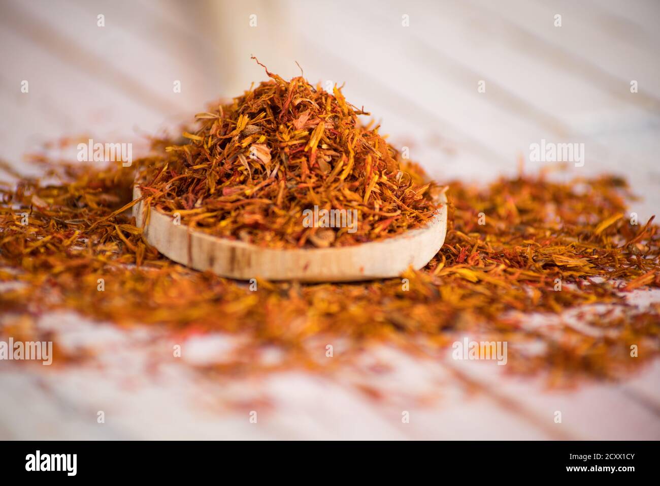 Primo piano di Safflower essiccato in cucchiaio di legno su bianco rustico sfondo Foto Stock