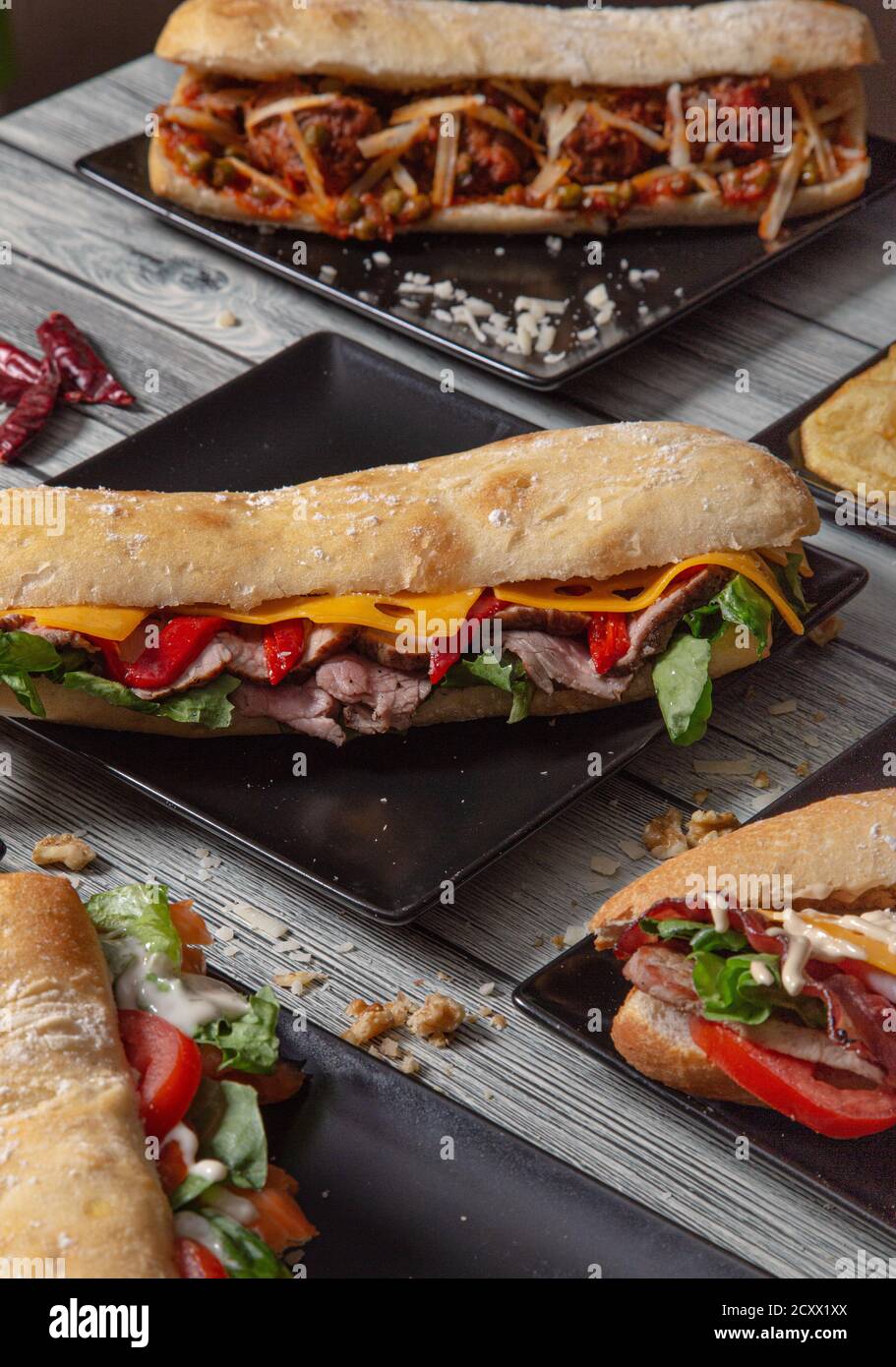 Panini Baguette con vari ingredienti serviti in piatti di ceramica su tavolo di legno. Immagine isolata. Varietà di panini Foto Stock