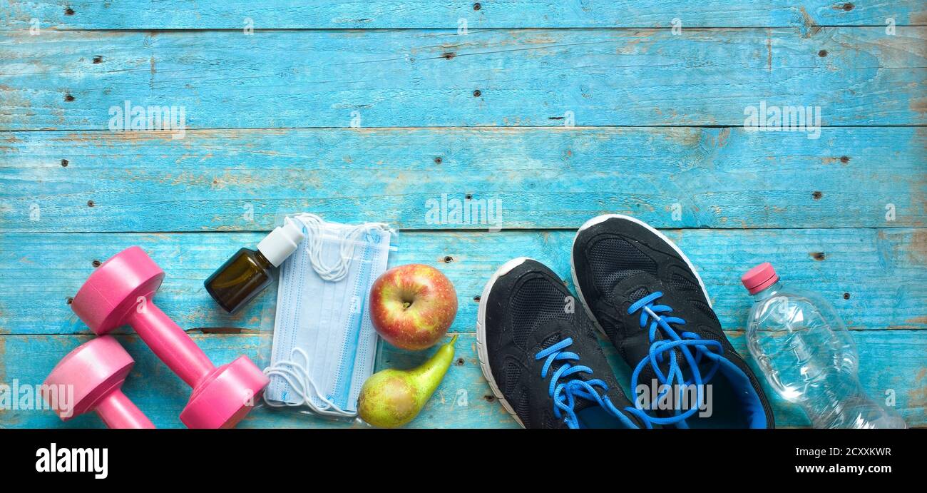 allenati in tempi di coronavirus; maschera corona, spray disinfettante, coppia di runner, manubri, acqua, mela, pera, cornavirus politica concetto Foto Stock