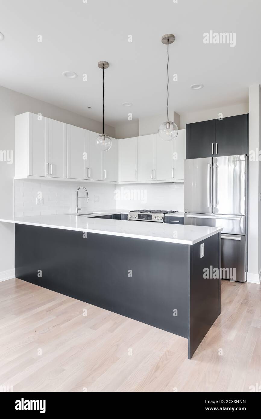 Una cucina in bianco e nero a due tonalità con luci appese sopra il piano di lavoro in marmo, elettrodomestici in acciaio inossidabile e piastrelle bianche della metropolitana. Foto Stock