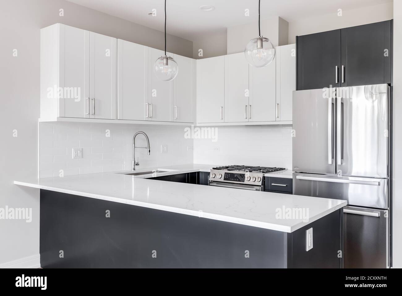 Una cucina in bianco e nero a due tonalità con luci appese sopra il piano di lavoro in marmo, elettrodomestici in acciaio inossidabile e piastrelle bianche della metropolitana. Foto Stock