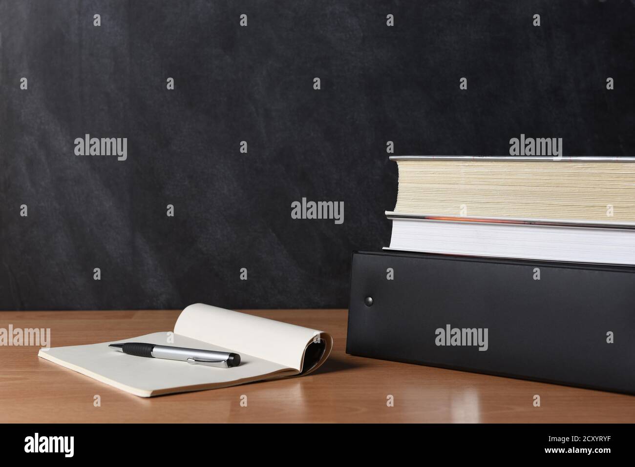 Scrivania per insegnanti con blocco note e penna e libri accatastati su un bunder. Foto Stock