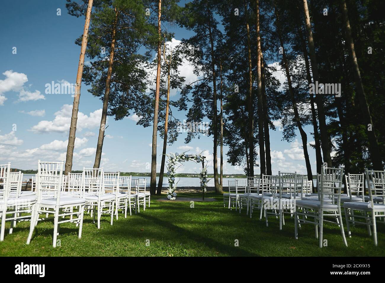Cerimonia nuziale all'aperto presso la costa del lago - matrimonio arco decorato con fiori freschi e sedie bianche vuote Foto Stock