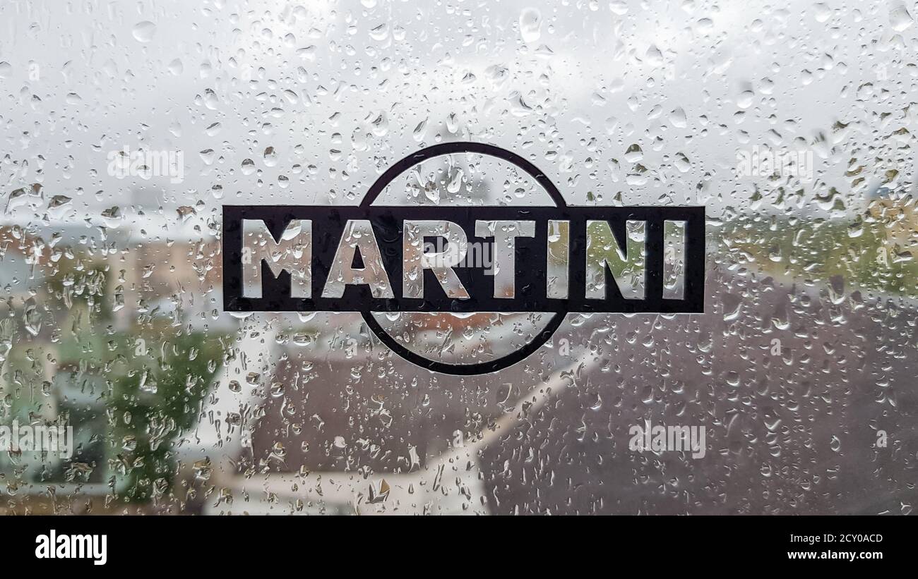 Logo adesivo Martini. Un marchio di vermut e spumanti italiani. Goccia d'acqua sulla finestra di vetro durante la pioggia con sfondo sfocato della città sc Foto Stock