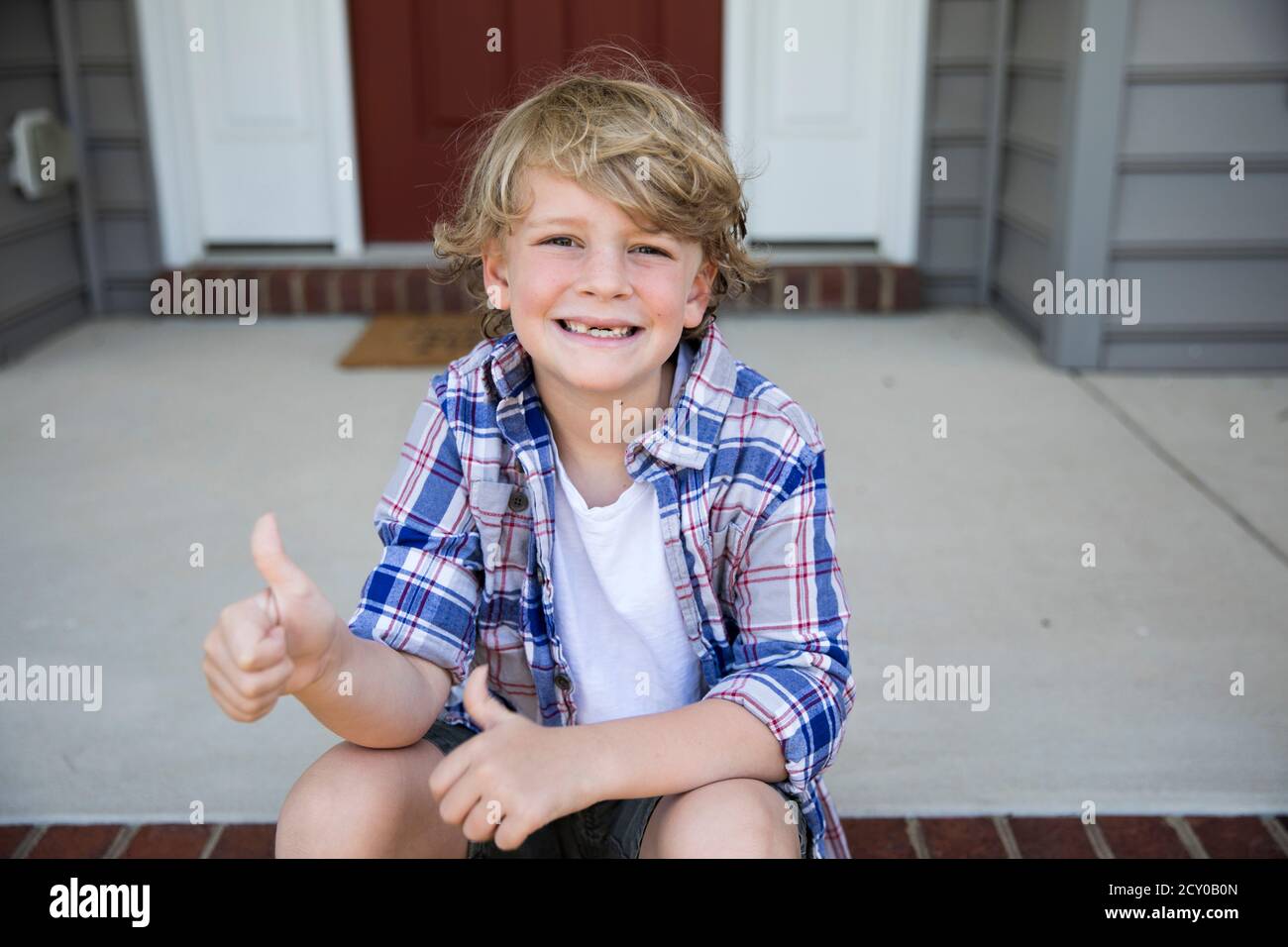 Il ragazzo di primo grado senza denti dà i thumbs in su mentre si siede sopra Scalini in mattoni Foto Stock