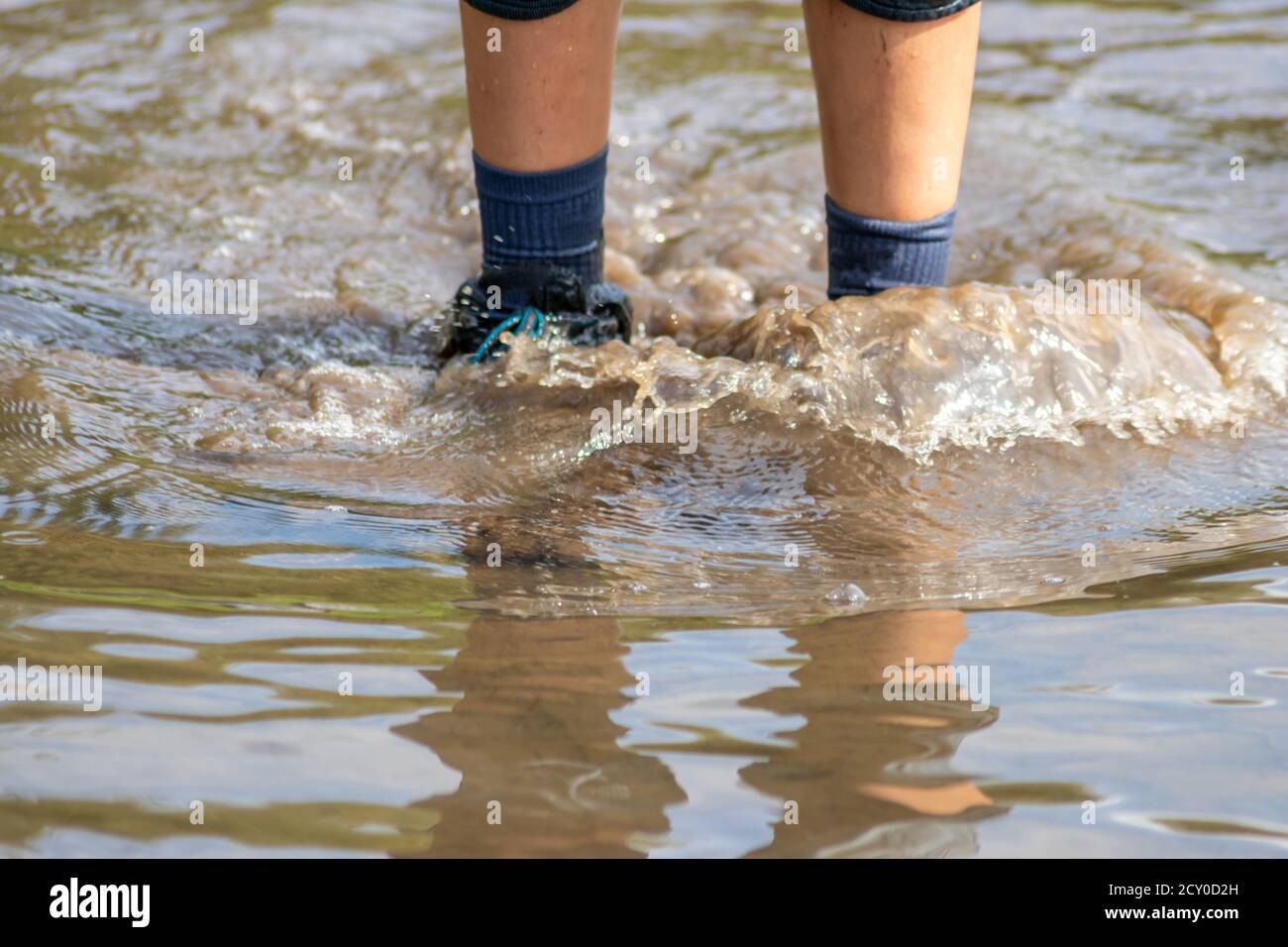 Ragazzo giovane che guidi attraverso l'alta marea con gumboot blu dopo un'alluvione ha rotto la diga di protezione e traboccante il paesi bassi o costa dell'oceano Foto Stock