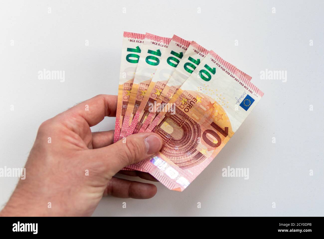 Mano di un uomo che detiene un mazzo di banconote da 10 euro come ricompensa, credito o reddito di lavoro secondario con un fondo bianco offuscato che mostra in somma 50 euro Foto Stock