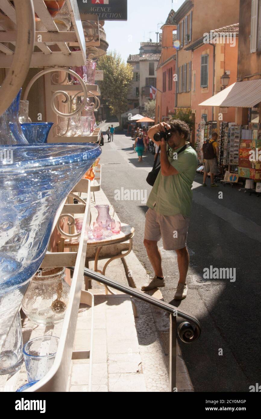 Sotto i negozi della strada del centro, i pezzi artistici sono realizzati in laboratori di soffiatura del vetro e collocati su scaffali e vetrine. Fotografo uomo dai capelli ricci Foto Stock