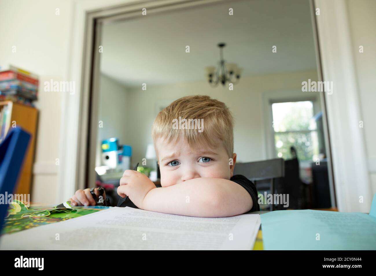 Ragazzo di età prescolare biondo seduto e pouting con mento riposante sul braccio Foto Stock