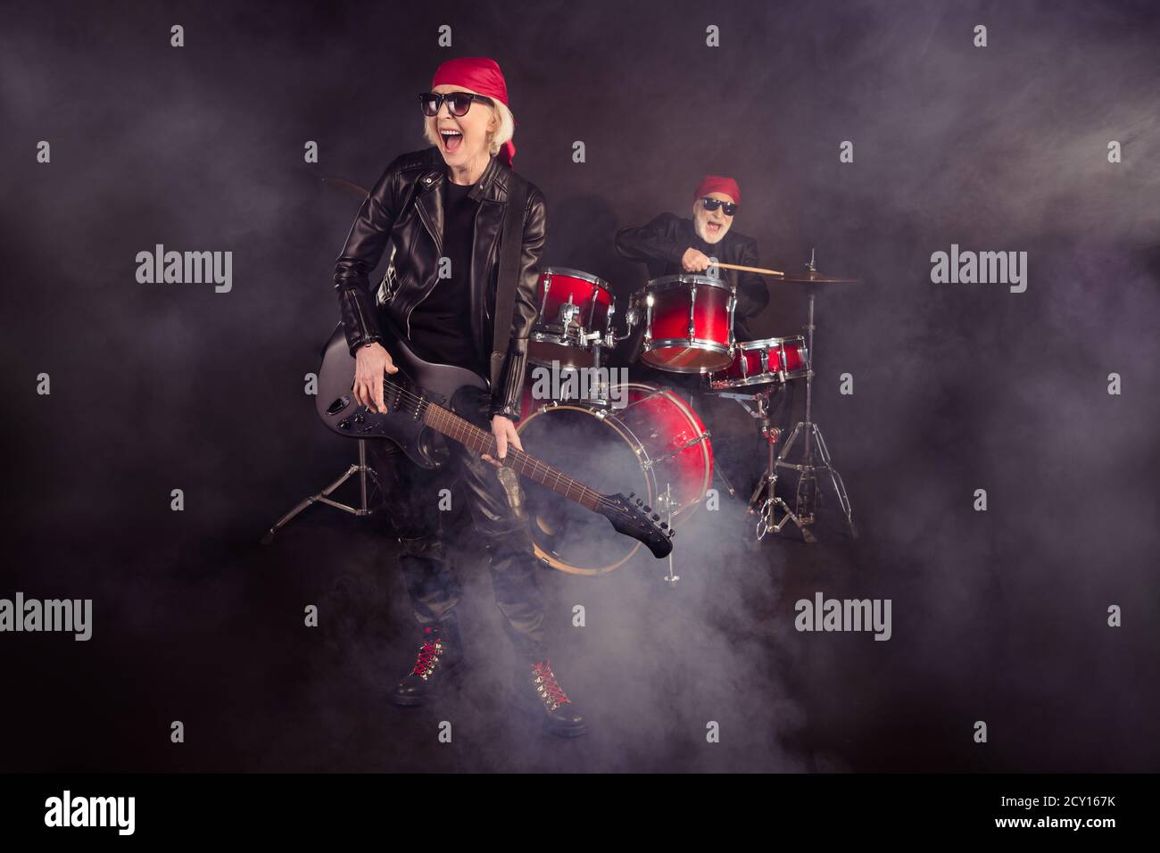 Foto a dimensione intera di due donne fresche invecchiate rock uomo gli  strumenti a batteria per concerti di gruppo suonano solo la chitarra fog in abbigliamento  elegante in pelle basculante air wear