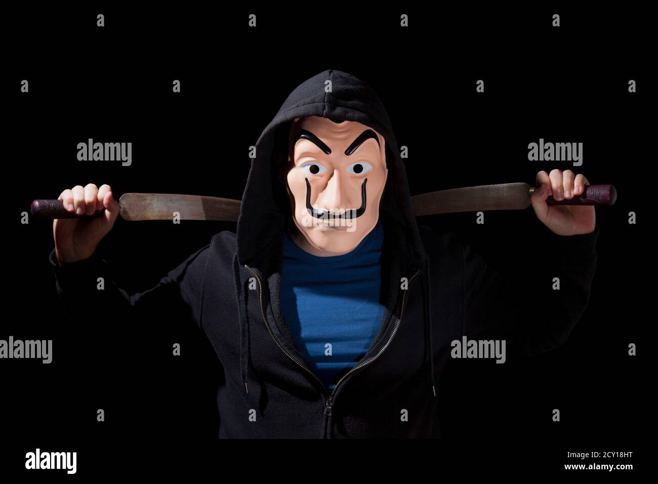 Uomo armato di machete e indossando una maschera e una felpa con cappuccio su sfondo nero. Foto Stock