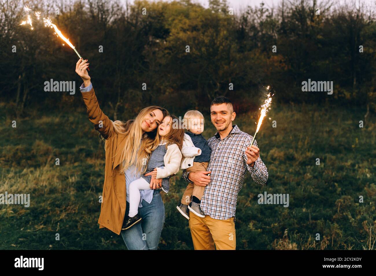 Ritratto di una famiglia felice con luci Bengala in un campo verde Foto Stock