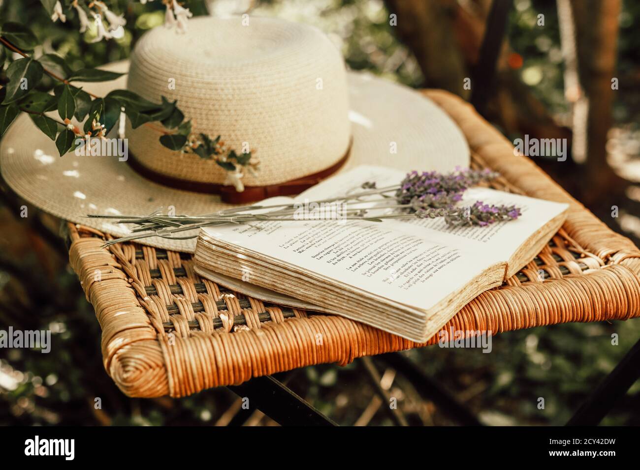 Bouquet di lavanda su libro aperto e cappello estivo femminile su vecchia sedia in vimini in giardino, natura e concetto di vita lenta Foto Stock