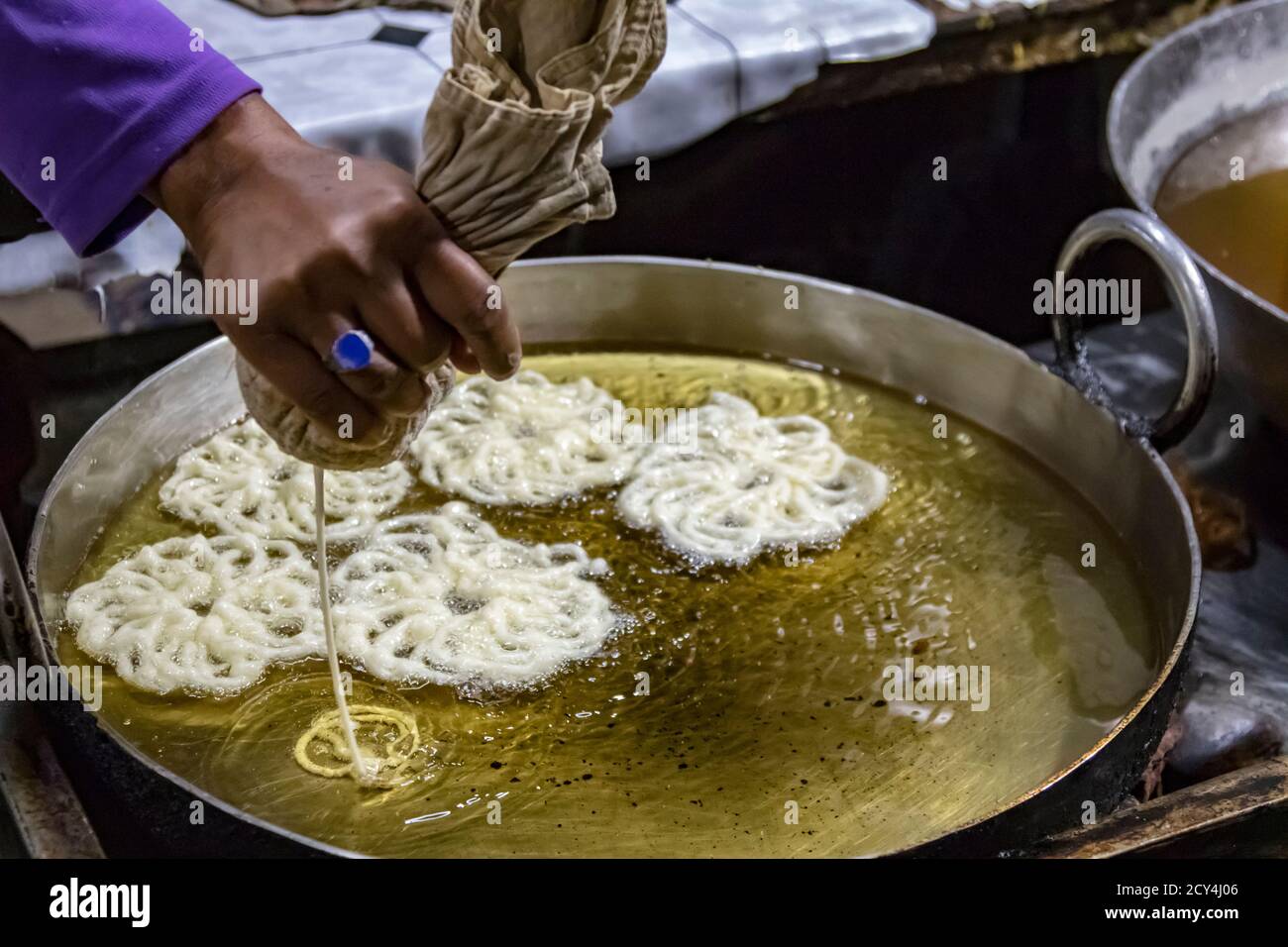 Visto mano versando la pasticceria in olio caldo per un pretzel-come snack presso un venditore ambulante Foto Stock