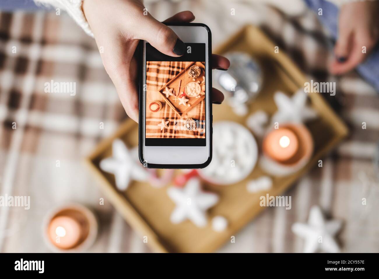 Mano femminile con smartphone scatta foto di Capodanno o Natale flatlay per i social network. Preparazione per le festività, creazione di contenuti. Legno tr Foto Stock