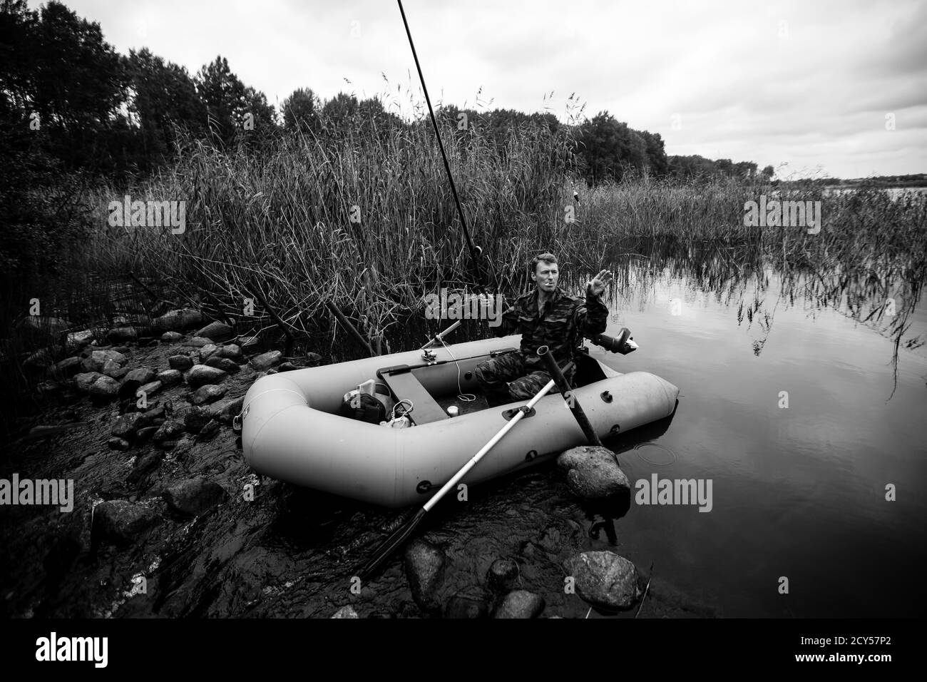 Pescatore su barca di gomma che cattura il pesce nel fiume d'estate. Fotografia in bianco e nero. Foto Stock