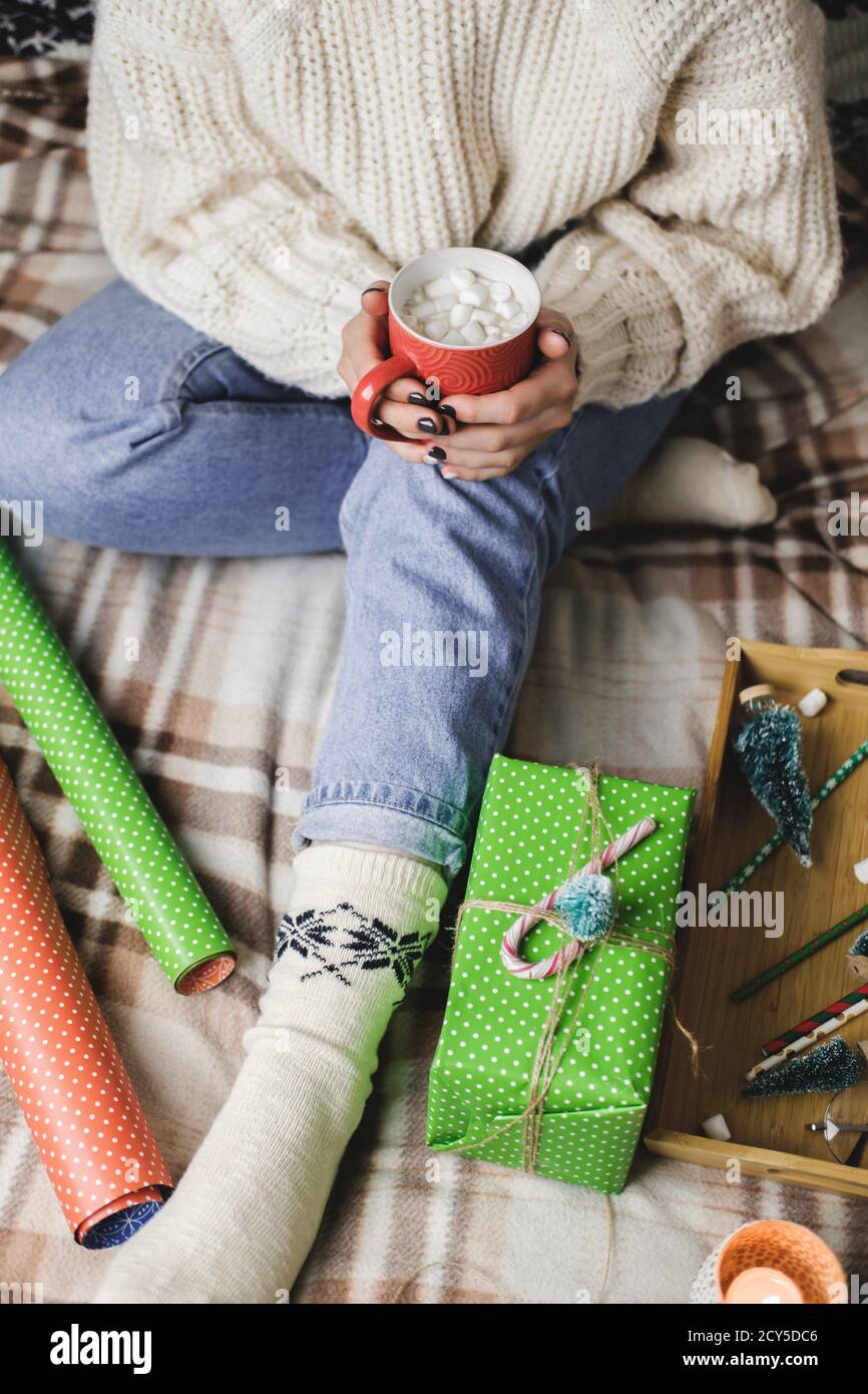 La giovane donna si siede sulla plaid in un comodo pullover bianco di lana lavorato a maglia e tiene una tazza di cacao con marshmallows. Higge Capodanno, preparazione per le vacanze. CAN Foto Stock