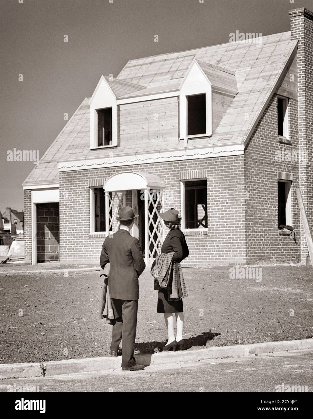 ANNI '30 1940 GIOVANE COPPIA UOMO DONNA MARITO MOGLIE VISTA POSTERIORE GUARDANDO LA NUOVA CASA IN COSTRUZIONE NELLO SVILUPPO DI ALLOGGI - S5180 HAR001 HARS FEMMINE SPOSATE CONIUGE MARITI COPIA VITA DOMESTICA SPAZIO FULL-LENGTH DONNE PERSONE MASCHI EDIFICI B&W PARTNER SVILUPPO SOGNI PROPRIETÀ GIOVANE UOMO ESTERNO A IN ACQUISTO BUYER IMMOBILIARE STRUTTURE EDIFICIO DI INVESTIMENTO MEDIO-ADULTO MID-ADULT UOMO MID-ADULT DONNA PROSPETTIVA DI TOGETHERNESS DUE MOGLI DI STORIA NERO E BIANCO ETNIA CAUCASICA HAR001 VECCHIO ALLA MODA Foto Stock