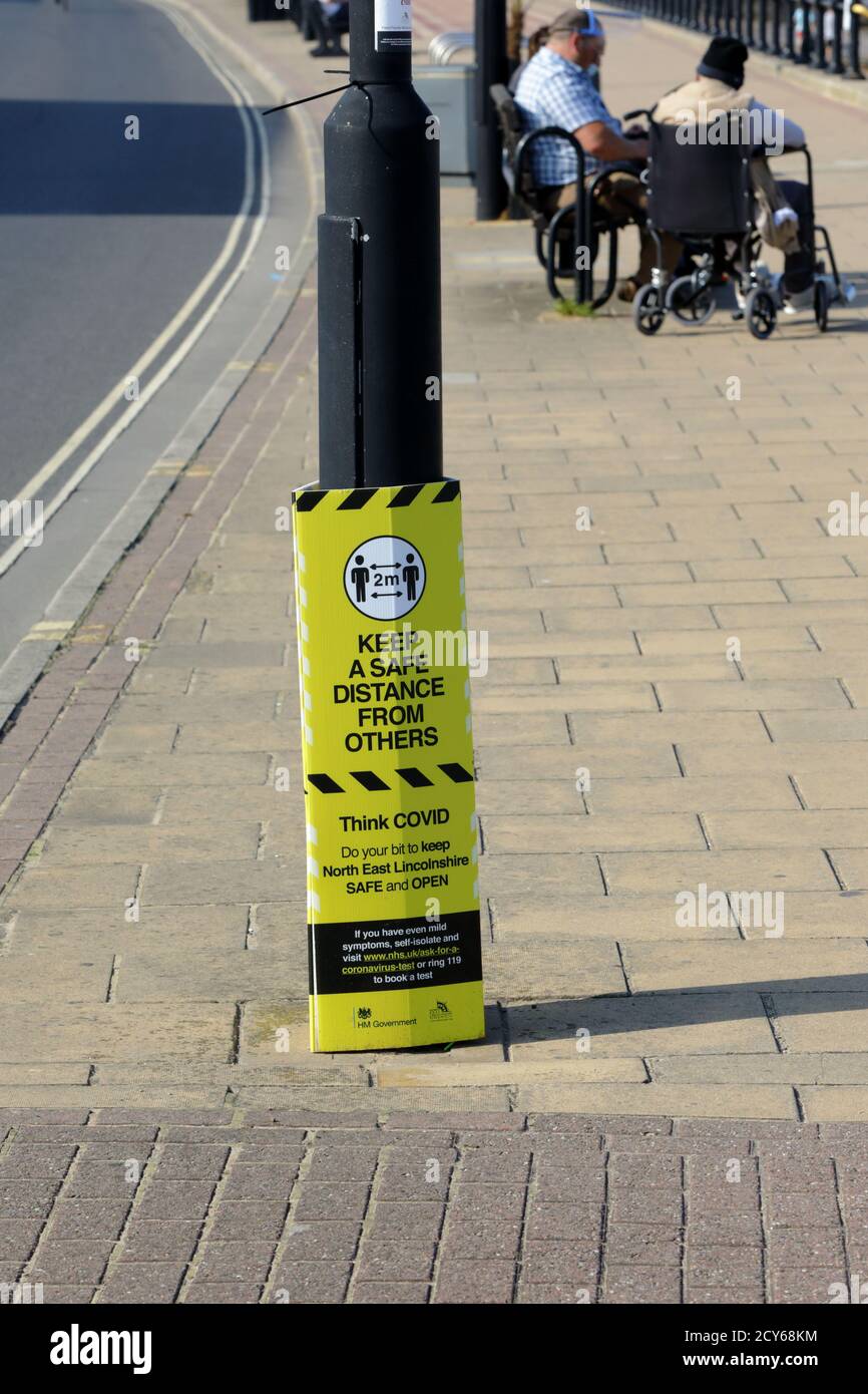 un segno giallo e nero fissato a un lampione avvertire le persone di mantenere una distanza sicura dagli altri Foto Stock