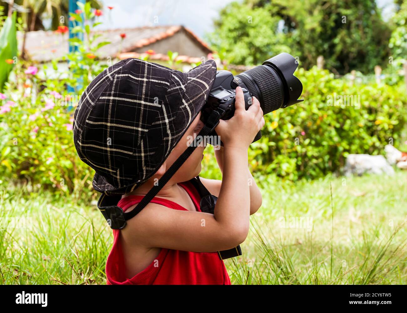 Vecchia fotocamera digitale tenuto da un piccolo bambino seduto sull'erba in giardino, sta sollevando la fotocamera come se stesse scattando una foto alla sua sinistra Foto Stock
