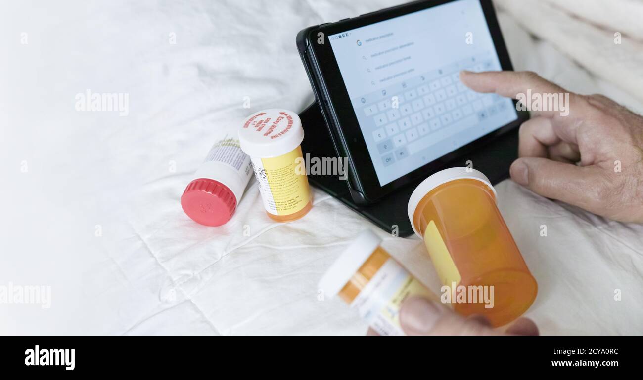 Una mano dell'uomo: Con il dito indice ha cercato informazioni su Internet utilizzando il suo tablet digitale. Pillole contenitori tutto intorno a lui (sulla coperta).. Foto Stock