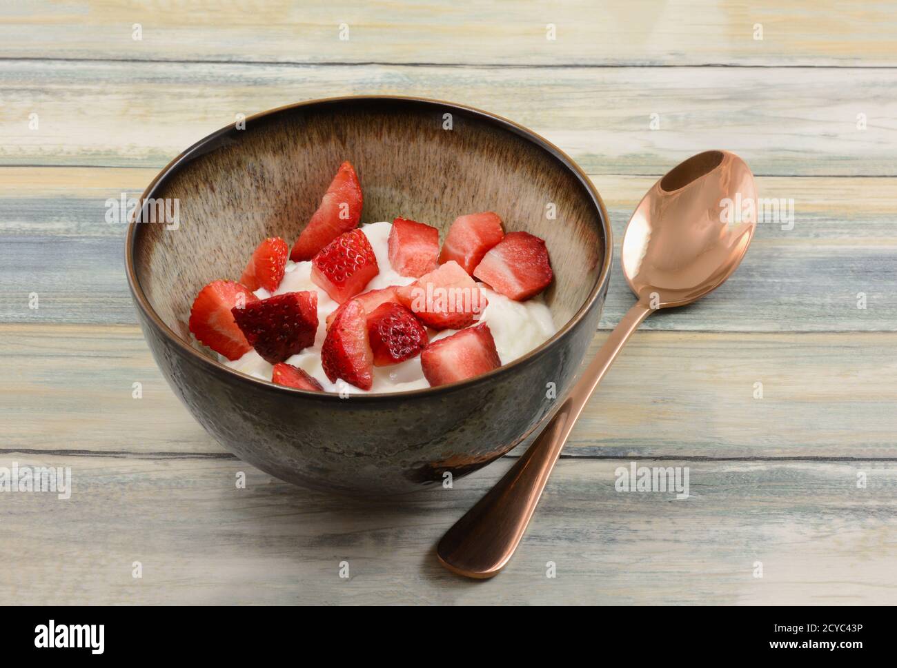 Fragole fresche tagliate e yogurt greco puro in recipiente con cucchiaio di rame Foto Stock