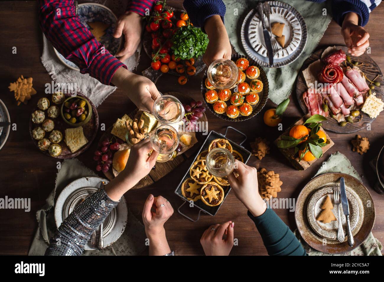 Gli amici sorseggiano un bicchiere con bevande per la cena di Natale o di Capodanno al tavolo delle feste. 2021 Foto Stock