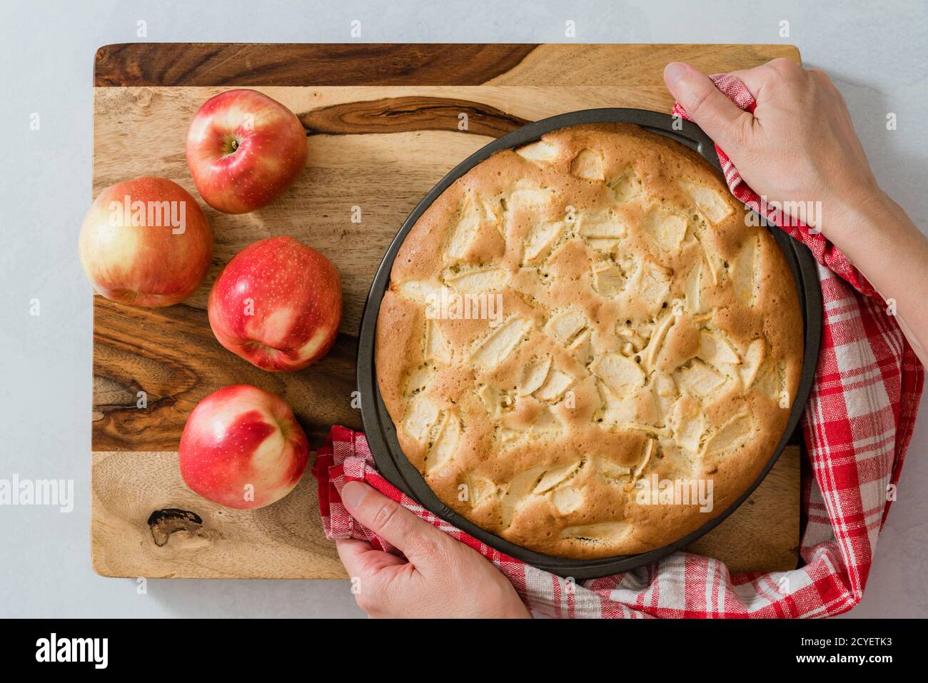 Torta di mele appena sfornata, morbida e umida, con mele a fette, primo piano su tavola di legno. Posa piatta, mani donna Foto Stock